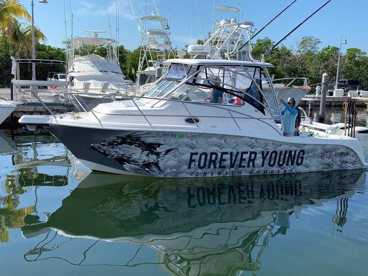 Express cruiser with a black and white fish wrap lettered Forever Young Charter Company