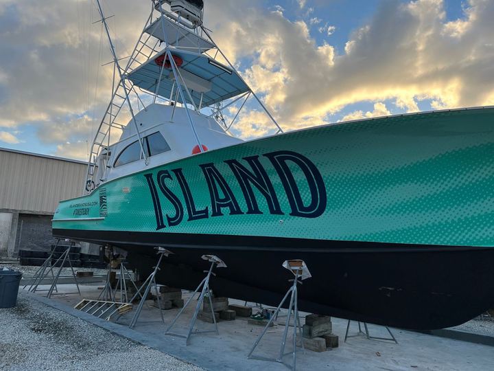 Sportfishing boat on stands with a teal hull wrap lettered ISLAND