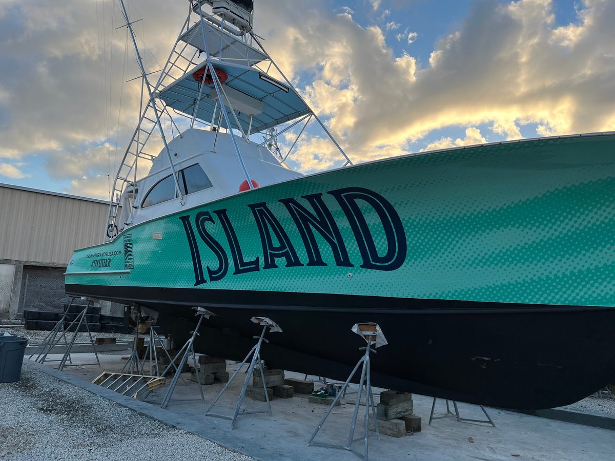 Sportfishing boat on stands with a teal hull wrap lettered ISLAND
