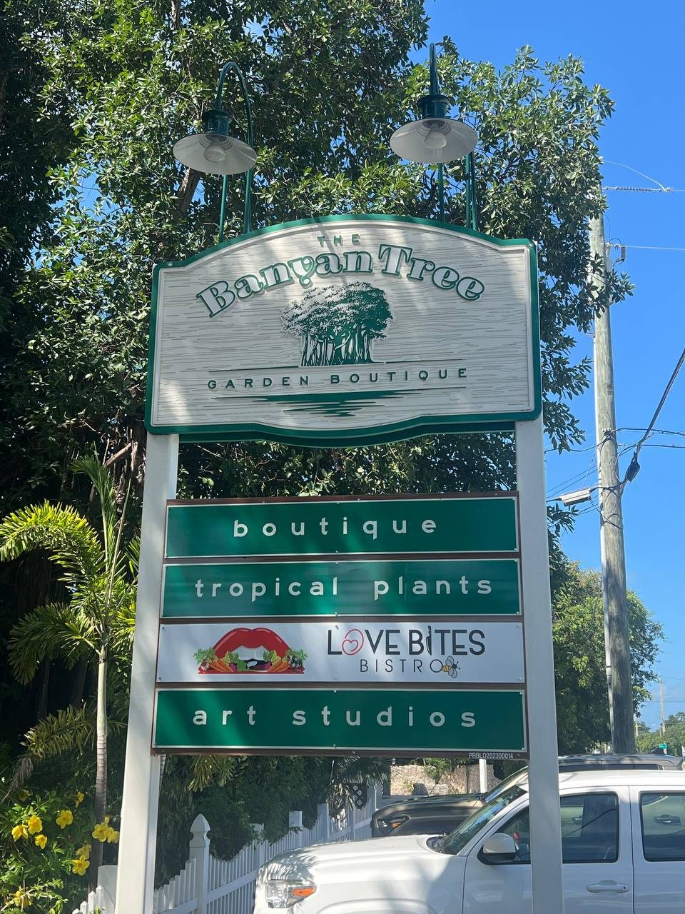 Carved Banyan Tree Garden Boutique sign with boutique, tropical plants, Love Bites Bistro and art studios panels