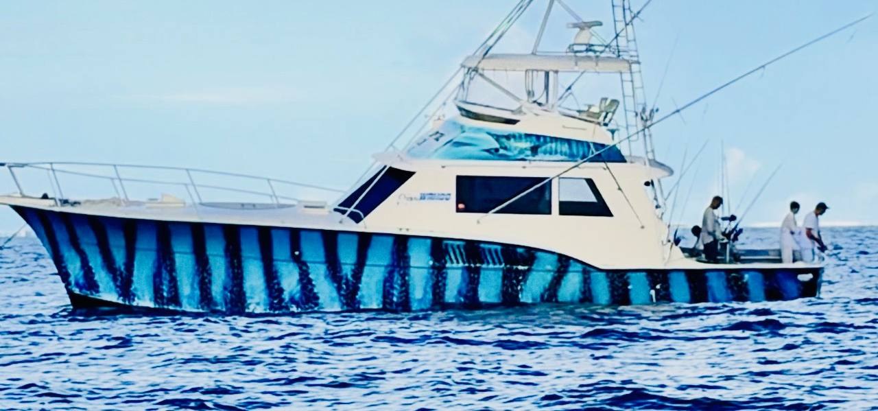 Sportfisher running offshore with a blue and black striped hull wrap, crew in the cockpit