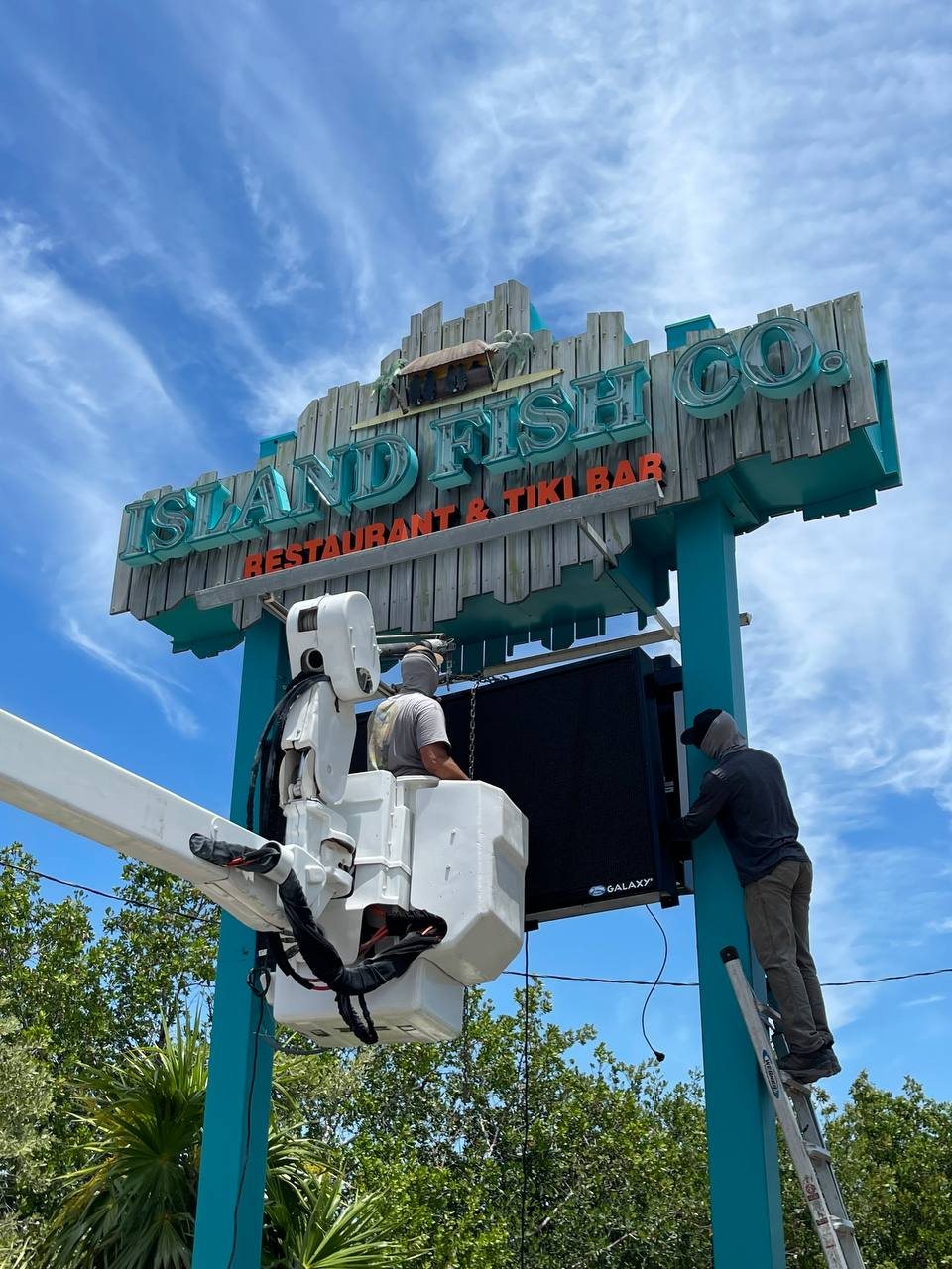 Our crew in the bucket and on a ladder installing an LED message board on the Island Fish Co. sign