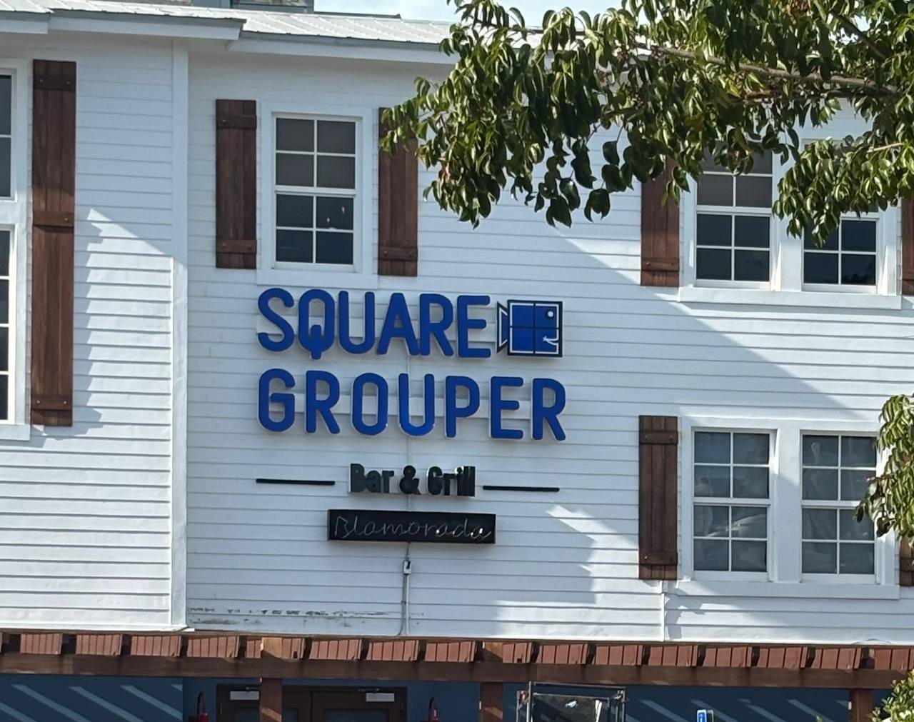 Square Grouper Bar and Grill blue raised letters on a white clapboard building