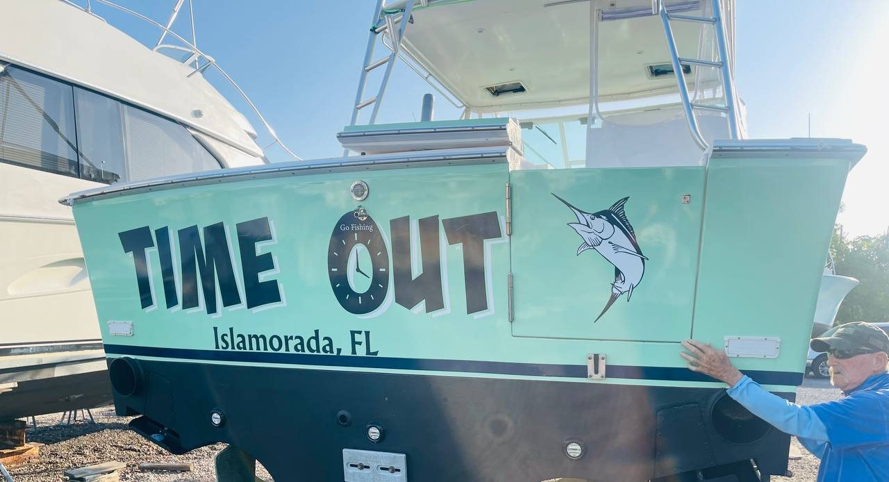 Installer applying Time Out Islamorada FL lettering and a marlin to a teal hull